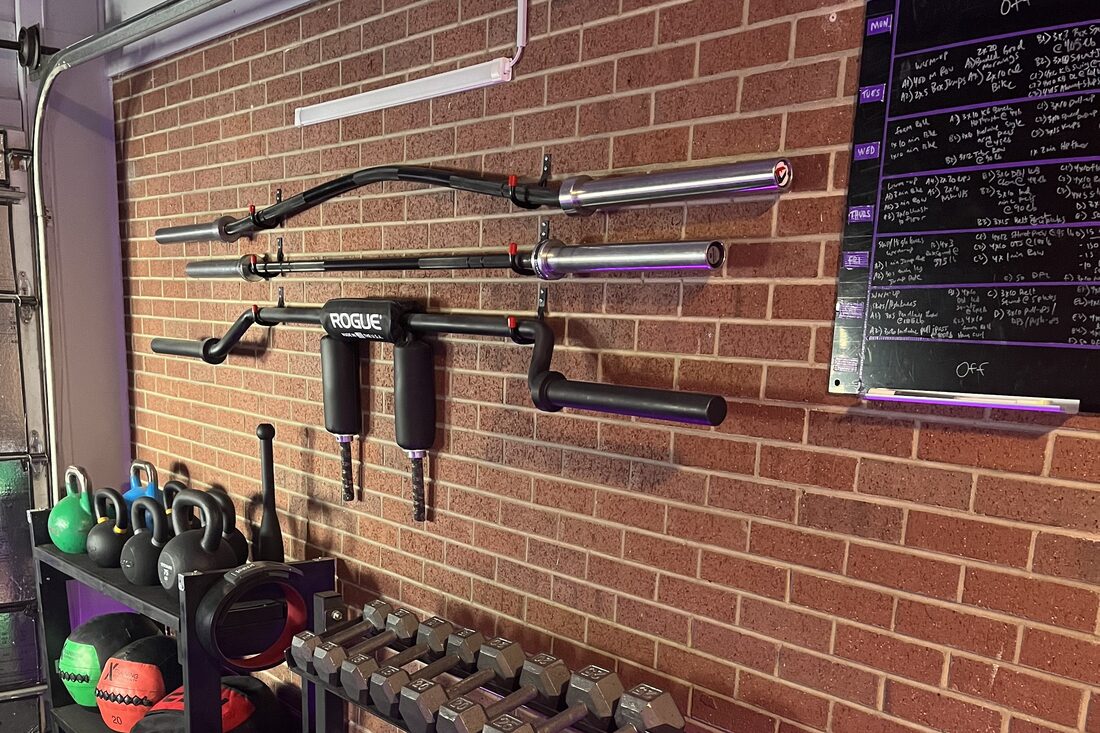 Specialty bars on the wall, kettlebells and dumbbells, and the week's programming on a whiteboard